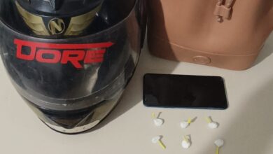 capacete de moto, duas cédulas de 20 reais, um aparelho celular e uma bolsa marrom em cima da mesa