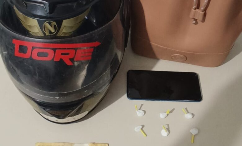 capacete de moto, duas cédulas de 20 reais, um aparelho celular e uma bolsa marrom em cima da mesa