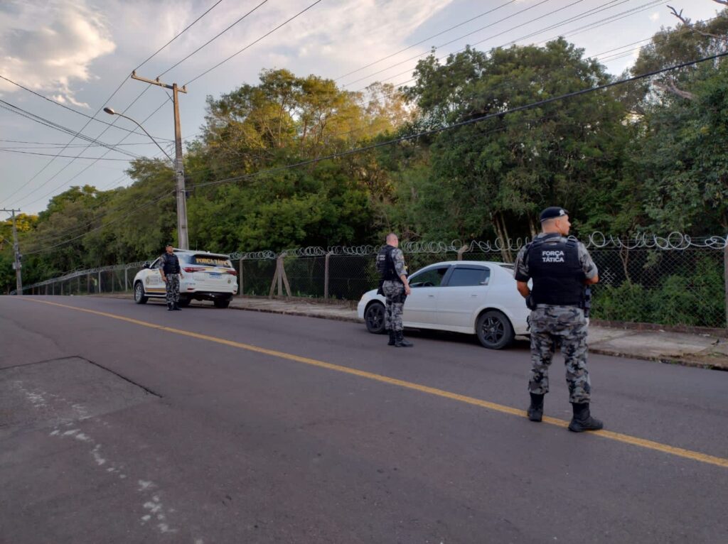 Dois carro estacionados, 3 policiais de costas com armas nas mãos