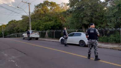 Dois carro estacionados, 3 policiais de costas com armas nas mãos