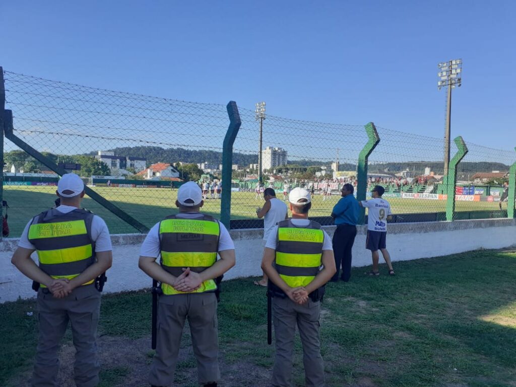 três policia de costa olhando para um campo de futebol