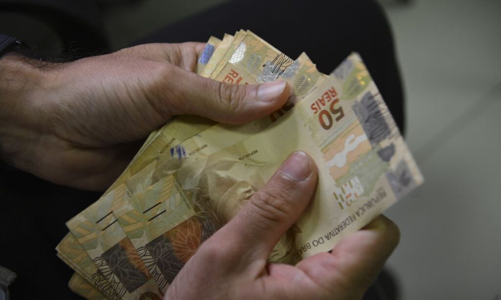 Mão segurando quatro notas de cinquenta reais